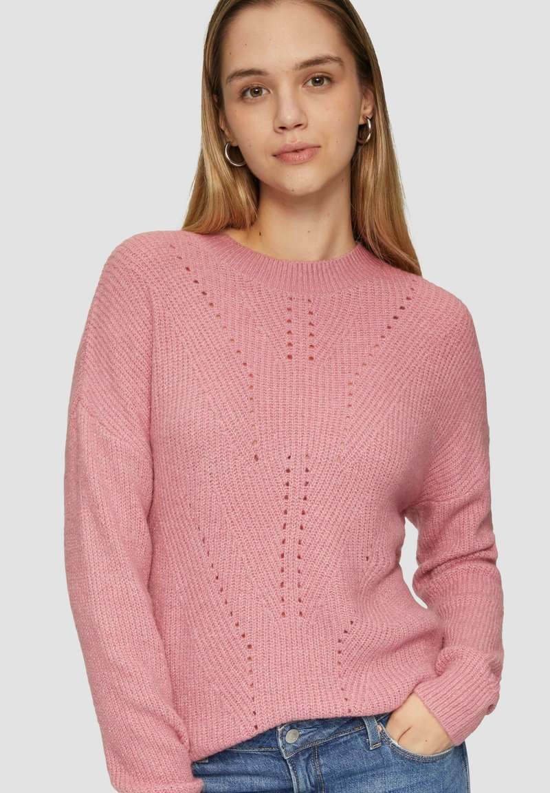 Pull en tricot rose avec un col rond, présentant un motif texturé et de petits détails découpés. Manches longues et coupe décontractée.