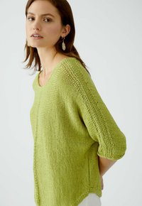 Light green knitted sweater with a loose fit, wide sleeves, and ribbed neck and hem details. The fabric features a textured pattern.