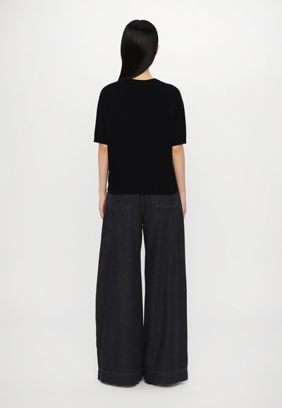 Black short-sleeve top paired with wide-leg dark denim pants. The fabric appears smooth, with a casual fit and no visible patterns or hardware.