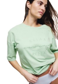 Mintgroene t-shirt met korte mouwen, voorzien van geborduurde tekst "RELAX en HERHAAL." Soepele textuur en relaxte pasvorm.