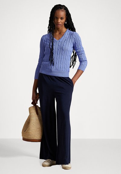 Light purple cable-knit sweater with a V-neck and three-quarter sleeves. Paired with navy wide-leg trousers and a woven tote bag.
