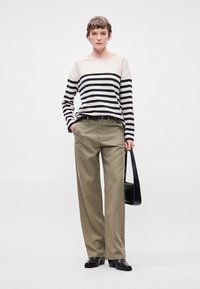 Ριγέ μπλούζα με μακριά μανίκια σε κρέμα και μαύρο, συνδυασμένη με παντελόνι καμπούρα σε χακί. Μαύρη ζώνη και τσάντα, λεία δερμάτινα παπούτσια ολοκληρώνουν την εμφάνιση.