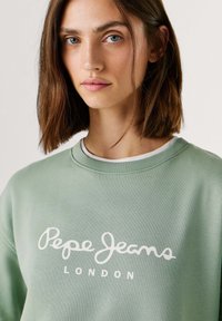 Πράσινο φούτερ με στρόγγυλη λαιμόκοψη, με λευκό λογότυπο "Pepe Jeans London" στο στήθος. Λείο ύφασμα και χαλαρή εφαρμογή.