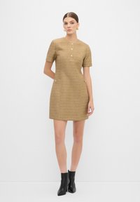 Kortärmad beige klänning med strukturerad stickad tyg, rund halsringning och gyllene knappar på framsidan och fickorna. Bärs med svarta ankelstövlar.