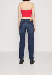 Mörkblå denimjeans med rak passform, fem fickor och en läderlogopatch på midjan. Toppdelen är en röd figurnära crop top.