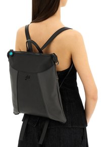 Zaino in pelle nera con finitura testurizzata, chiusura con zip e spallacci regolabili. Presenta un bottone accentato blu vicino alla parte superiore.