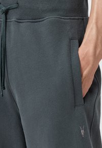 Donkergrijze sweatpants met een trekkoord in de taille, zijzakken en een klein geborduurd logo van een geitenkop. Zachte, textuurstof.