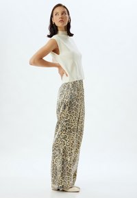Witte mouwloze top en beige panterprint wijde broek. Zachte textuur, hoge halslijn en gedurfde dierenprint creëren een opvallend contrast.