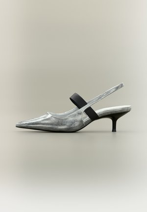 Chaussure slingback argentée à bout pointu avec un petit talon kitten noir et une bride élastique noire sur le dessus.