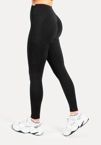 Leggings neri a vita alta in tessuto elastico, con dettaglio testurizzato sul retro, abbinati a sneakers sportive bianche.
