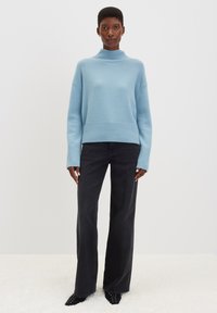 Maglione azzurro chiaro a coste con colletto a dolcevita e spalle scese, abbinato a jeans neri a gamba larga. Il maglione presenta una finitura texturizzata e un fit rilassato.