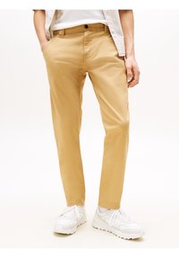 Beżowe chino o wąskim kroju, wykonane z bawełny, z bocznymi kieszeniami i zapięciem na guzik. Stylizowane z białymi trampkami.