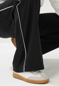 Pantalones negros con ribete lateral blanco, combinados con zapatillas ligeras en gris y blanco que cuentan con una suela de goma, tejido texturizado y diseño con cordones.