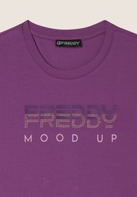 T-shirt corto viola realizzato in misto cotone. Presenta la scritta "FREDDY" in viola scuro con dettagli in borchie e "MOOD UP" in rosa chiaro.