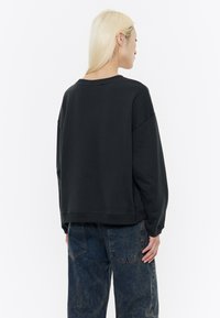 Felpa nera, oversize, con spalle scese e colletto a costine. Realizzata in morbido tessuto, presenta una vestibilità comoda e un orlo dritto.