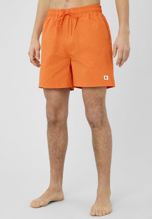 Homme portant un short de bain texturé orange vif avec taille élastique et cordon de serrage, debout pieds nus sur un fond uni.
