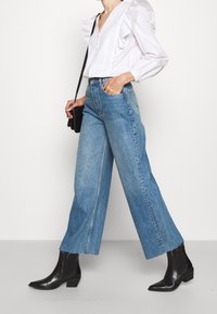 White blouse with ruffled details, high-waisted light blue denim wide-leg jeans, and black ankle boots with a slightly pointed toe.