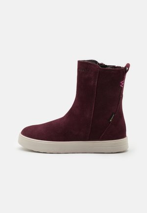 Botte mi-mollet en daim bordeaux avec une semelle en caoutchouc blanche, une languette à l'arrière et un logo de marque discret près du haut et sur le côté.