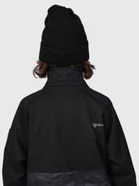 Persona que lleva un gorro de punto negro y una chaqueta negra con un alto cuello, de espaldas frente a un fondo gris liso.