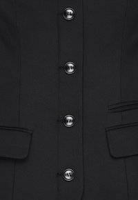 Blazer nero in tessuto texture, con sei bottoni neri lungo la parte anteriore e due tasche laterali. Design su misura e strutturato.