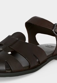 Δερμάτινο ανδρικό σανδάλι σκούρου καφέ χρώματος με ανοιχτό σχέδιο στη μύτη, φαρδιές λουρίδες και ρυθμιζόμενο κούμπωμα σε μαύρη σόλα.