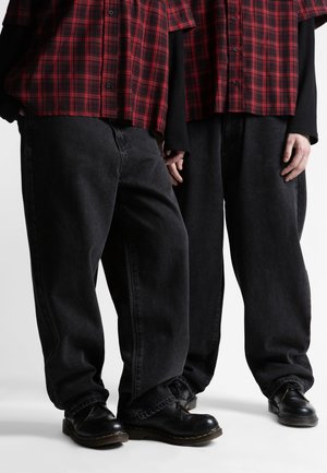 To personer iført sorte lædersko, løstsiddende sorte jeans og røde og sorte ternede skjorter over sorte langærmede bluser.