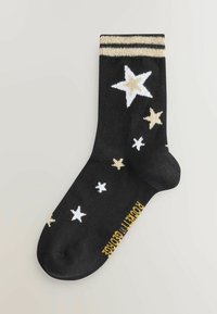 Schwarze Socken mit weißen und goldenen Sternmustern, einem gestreiften goldenen Band am oberen Ende und einem goldenen Textdetail nahe der Fußsohle.