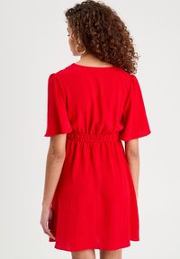 Robe rouge avec des manches courtes, une taille élastique et une jupe évasée. Le tissu semble léger et doux avec une finition texturée.