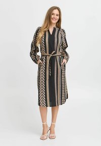 Rochie neagră cu modele geometrice aurii și roz, mâneci lungi, curea cu nod și buzunare laterale; confecționată dintr-un material ușor.