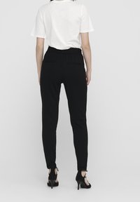 Zwarte tapered broek met een elastische tailleband en achterzakken, gecombineerd met een wit T-shirt met korte mouwen en zwarte hoge hakken.