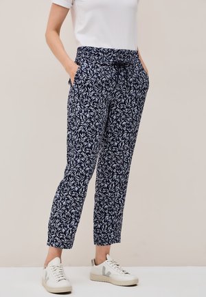Navy trousers with a white leafy pattern, elastic waistband, and side pockets, paired with white sneakers. Lightweight fabric, relaxed fit.