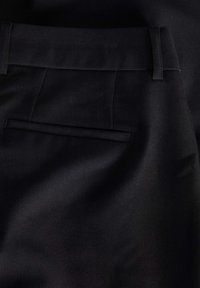 Svarta skräddarsydda byxor med en slät tygtextur, veckdetaljer och en enda bakficka med en dold klaff.