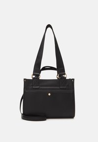 Czarna prostokątna torebka na ramię z szerokimi paskami, krótkimi uchwytami i małym złotym heksagonalnym emblematem na przedniej kieszeni.