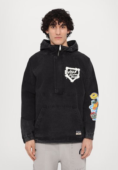 Jachetă din denim neagră cu glugă și un buzunar frontal, având un logo alb și patch-uri colorate pe mânecă dreaptă. Mansete elastice la încheieturi.