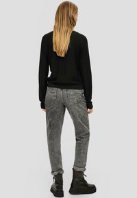 Schwarzer gestrickter Pullover mit langen Ärmeln, kombiniert mit grauen Jeans. Die Stiefel sind schwarz mit einer strukturierten Oberfläche. Einfaches, lässiges Outfit.