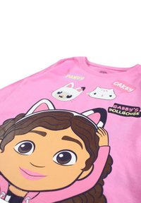 T-shirt en coton rose présentant un personnage de dessin animé aux cheveux bouclés et des accents d'oreilles de chat, accompagné de graphismes de deux animaux dessinés et de texte.