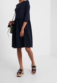 Abito blu navy con top aderente e gonna a campana, realizzato in tessuto morbido. Abbinato a sandali con piattaforma neri dotati di cinturini regolabili.