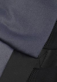 Zbliżenie na ciemnoniebieską tkaninę przeplatającą się z czarną siateczką oraz przeszytym czarnym paskiem.