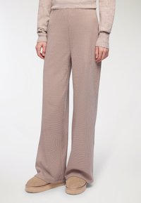 Szerokie, wysokie spodnie w kolorze miękkiego beżu, z prążkowaną teksturą i subtelnym wzorem w kratę, połączone z tanimi butami wsuwanymi.