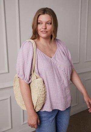Blusa lilás xadrez com decote em V, mangas bufantes e detalhe de botão; modelo segura uma bolsa de ombro tecida de forma natural.