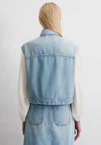 Lichtblauwe denim mouwloze jas met een aansluitende taille en achterzakken. Zachte textuur en een schoon, klassiek ontwerp.
