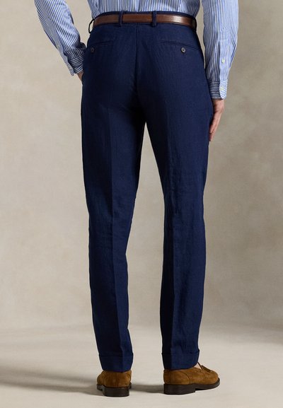 Marineblå linbukser med rett snitt, med to baklommer og en subtil tekstur. Kombinert med brune semskede sko, sett bakfra.