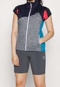 Grå zip-väst med marinblå, rosa och turkosa accenter; texturerad framsida, hög krage, korta ärmar. I kombination med grå cykelshorts.