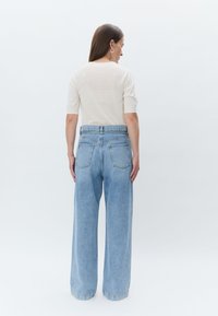 Un haut tricoté beige clair à manches courtes associé à un jean large taille haute bleu clair avec deux poches arrière.