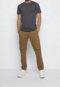 Grå t-shirt med korte ærmer, parret med brune cargo bukser med flere front lommer. Hvide sneakers fuldender outfittet.