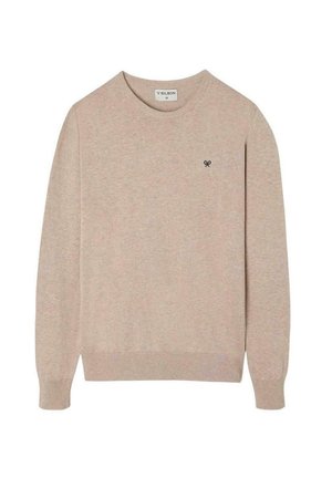 Suéter tejido beige con un cuello redondo, mangas largas, puños acanalados y un pequeño emblema oscuro en el pecho. Textura suave.
