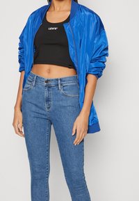 Giacca bomber in satin blu, top corto nero con logo bianco e jeans di denim leggero azzurro aderenti, con classico design a cinque tasche e leggero stretch.