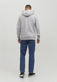 Felpa grigia con tasca a canguro e cappuccio regolabile, abbinata a jeans denim blu e sneakers nere, vista da dietro.