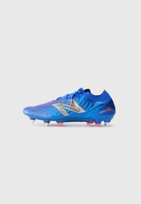 Blue soccer cleat with textured synthetic upper, silver logo, and pink accents. Features four white studs for traction on grass surfaces.
