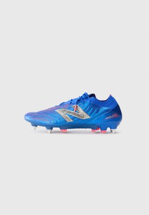 Blue soccer cleat with textured synthetic upper, silver logo, and pink accents. Features four white studs for traction on grass surfaces.